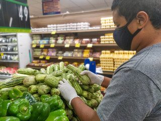 Black man choosing zucchini with glove, protection against coronavirus
