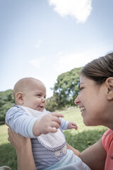 Bebé varón con su mamá en un parque riendo y sonriendo mirándose uno al otro