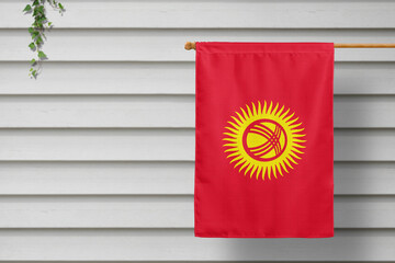 Kyrgyzstan national small flag hangs from a picket fence along the wooden wall in a rural town....