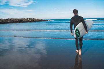 surfer entering into the water with his surfboard.
