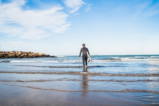 Surfer entering into the water with his surfboard. - Powered by Adobe