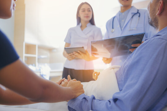 Doctor And Nurse Talk With Husband Patient About Examining Result From Doctor, Family Health Care, Palliative Care, With Wife Holding Hand Of Patient At Hospital. Selected Focus