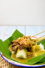 Sate padang is a traditional food satay beef from Padang Indonesia, completed with lontong, a traditional rice cake, and yellow special seasoning sauce on a traditional plate isolated on blue table