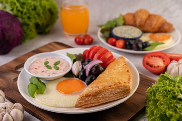 Breakfast consists of bread, fried egg, salad dressing, black grapes, tomatoes, and sliced ​​onions.