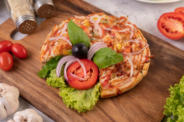 Fototapeta na wymiar The pizza is in a wooden tray topped with red onions, black grapes, tomatoes, and lettuce.
