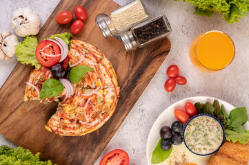The pizza is in a wooden tray topped with red onions, black grapes, tomatoes, and lettuce.