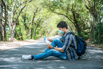 Male tourists sit and look at the map on the road.