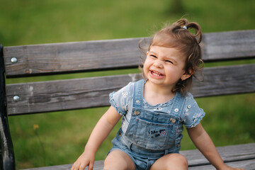 Adorable little girl laughing. Beautiful female kid in denim sitting on the bench in park. Happy little girl smile. Eighteen month