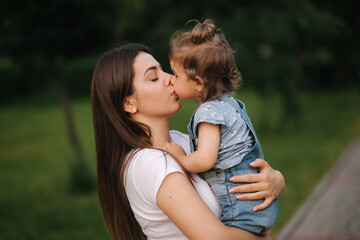 Portrait of beautiful mom with adorable little girl. Happy family outdoors. Daughter give kiss to mom