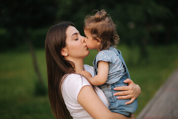Fototapeta premium Portrait of beautiful mom with adorable little girl. Happy family outdoors. Daughter give kiss to mom