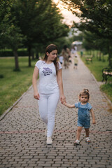 Beautiful young mom walkin in park with her adorable little daughter. Cute little girl hom mothers's hand