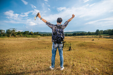 A male traveler with a backpack carrying a map and standing on the meadow.