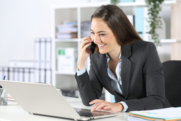Happy executive calls on phone using laptop at office