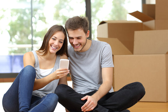 Happy couple moving home checking phone with boxes