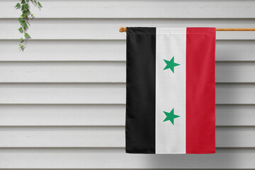 Syria national small flag hangs from a picket fence along the wooden wall in a rural town....