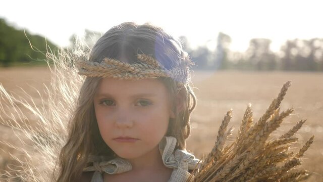serious sad girl a child stands on a wheat mown field with a rim of ears on his head