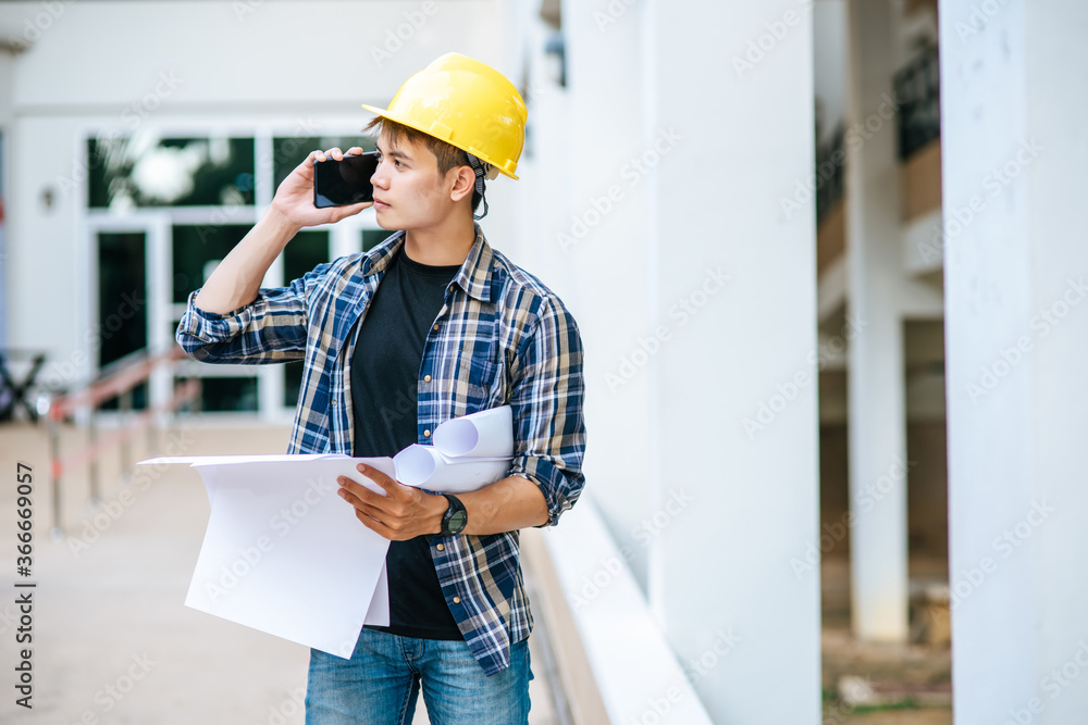 Wall mural architects hold floor plans and talk on the phone.