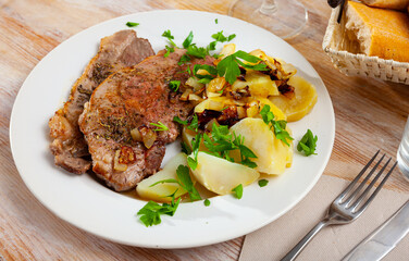 Close up of delicious baked pork with potatoes and greens, served on plate..