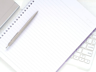 Flat lay white office desktop with blank notebook and pen put on the keyboard. Top view with space for text. Flat lay, Business and education concept...