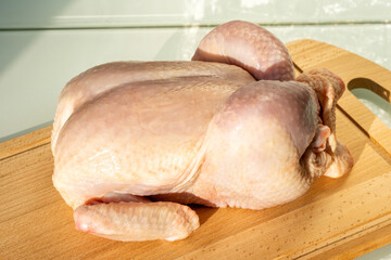 large raw chicken on wooden board