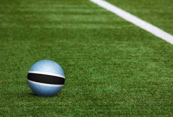 Botswana flag on ball at soccer field background. National football theme on green grass. Sports competition concept.