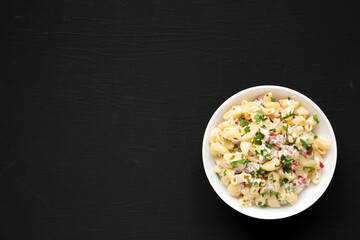 Homemade Macaroni Salad in a white bowl on a black background, top view. Flat lay, overhead, from above. Copy space.