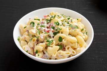 Homemade Macaroni Salad in a white bowl on a black background, side view. Close-up.