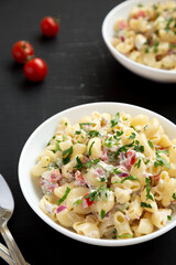 Homemade Macaroni Salad in a white bowl on a black background, side view.