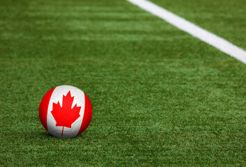 Canada flag on ball at soccer field background. National football theme on green grass. Sports...