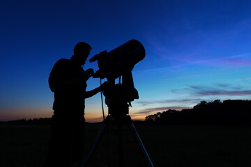 silhouette of a man setting up a telescope for night observation on dark blue sky at dusk