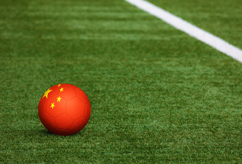 Fototapeta na wymiar China flag on ball at soccer field background. National football theme on green grass. Sports competition concept.