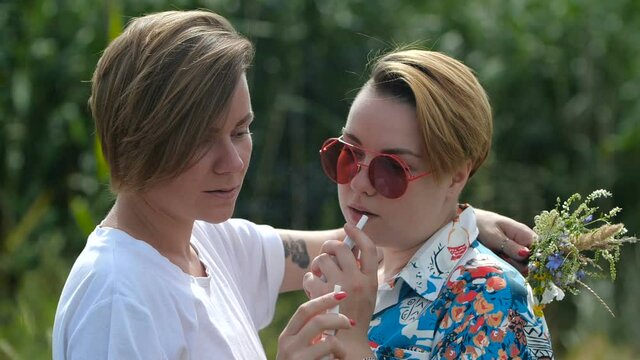 Close up same-sex couple smoking electronic cigarette. Two stylish lesbian girls smoke outdoors on summer sunny day. Slow motion 200 fps