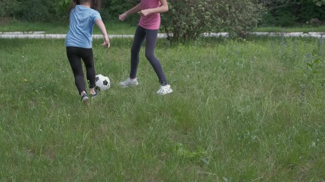 Children play football. Little sisters play football in the park on the green grass.