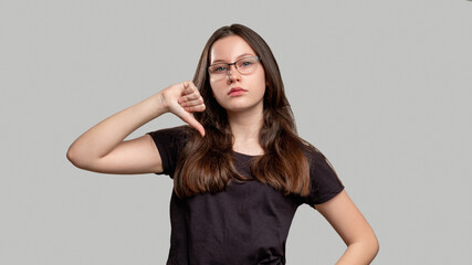 Dislike gesture. Bad idea. Arrogant woman showing disagreement with thumb down isolated on gray...