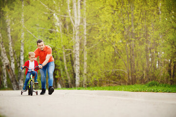Dad teaches little son to ride bike in park, keep balance, have fun family. Father day concept