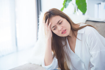 Beautiful asian woman sitting in living room with unhappy face .Woman having headache from migraine.