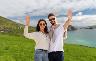 travel, tourism and vacation concept - happy couple waving hands over ireland on background