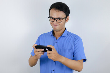 Fototapeta premium Asian young man enjoy and smile on the smartphone when play game. Indonesian man wearing blue shirt.