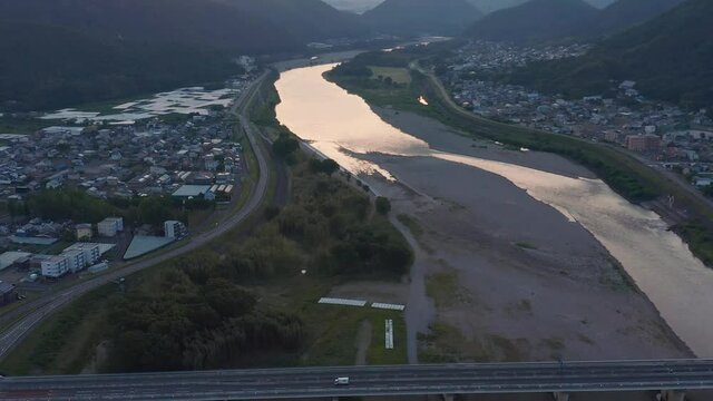 Aerial tilt revealing Nagara river in Gifu as car crosses bridge at sunrise