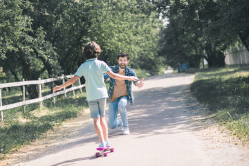 Dark-haired boy riding a skateboard, his father catching him