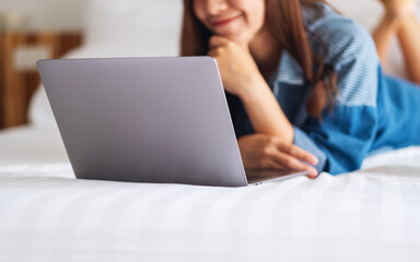 A beautiful asian woman using and working on laptop computer while lying down on a white cozy bed at home