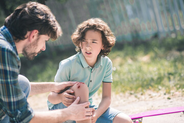 Man in a checkered shirt examining his sons injured knee