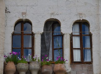 Fototapeta na wymiar Three arched windows in a row with flower pots on sills and sheer curtains blowing in the breeze