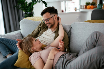 Husband and wife enjoying on sofa. Happy couple relaxing in living room.	