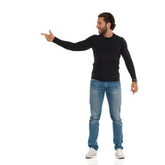 Handsome Man In Black Blouse And Jeans Is Looking Away And Pointing At The Side
