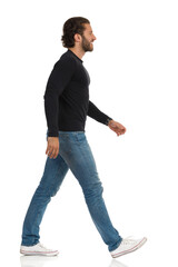 Handsome Man In Black Jersey, Jeans And Sneakers Is Walking And Looking Away. Side View.