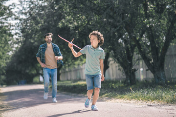Obraz premium Dark-haired boy running with a toy airplane, his father running after him