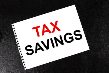 A WHITE sheet of paper with the text TAX SAVINGS. Tax concept. Close-up. On a black background.
