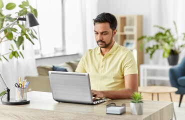 technology, remote job and lifestyle concept - indian man with laptop computer working at home office