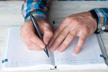 Pen in hand. The hand of a businessman writes in a notebook. On the table
